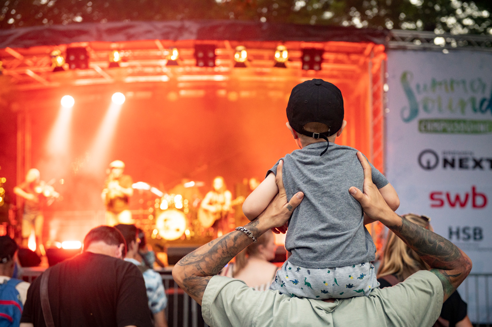 Kind auf den Schultern eines Erwachsenen beim Konzert
